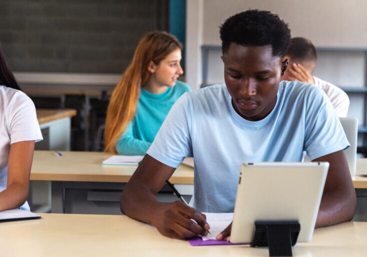 Teen black male student using digital tablet in class. African American high school male student doing homework. Copy space. Education concept.